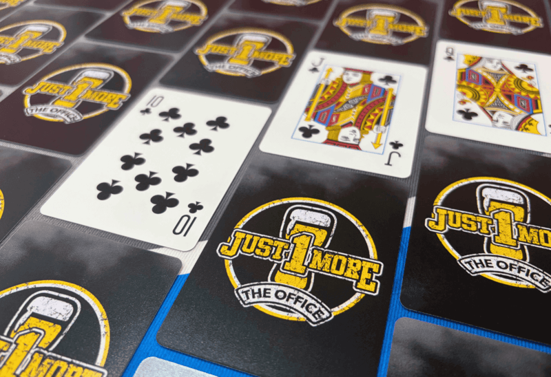 Playing cards with 'Just 1 More' logo on a branded card holder.